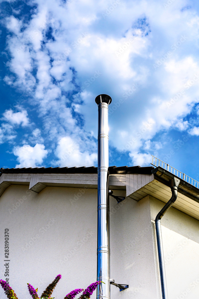 Stainless steel chimney and parts of a house in front of a bright blue sky with clouds.