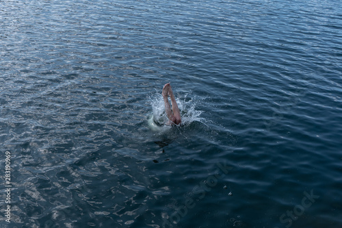 A young man dives into the blue water from a cliff on a hot summer day. Legs are out of water