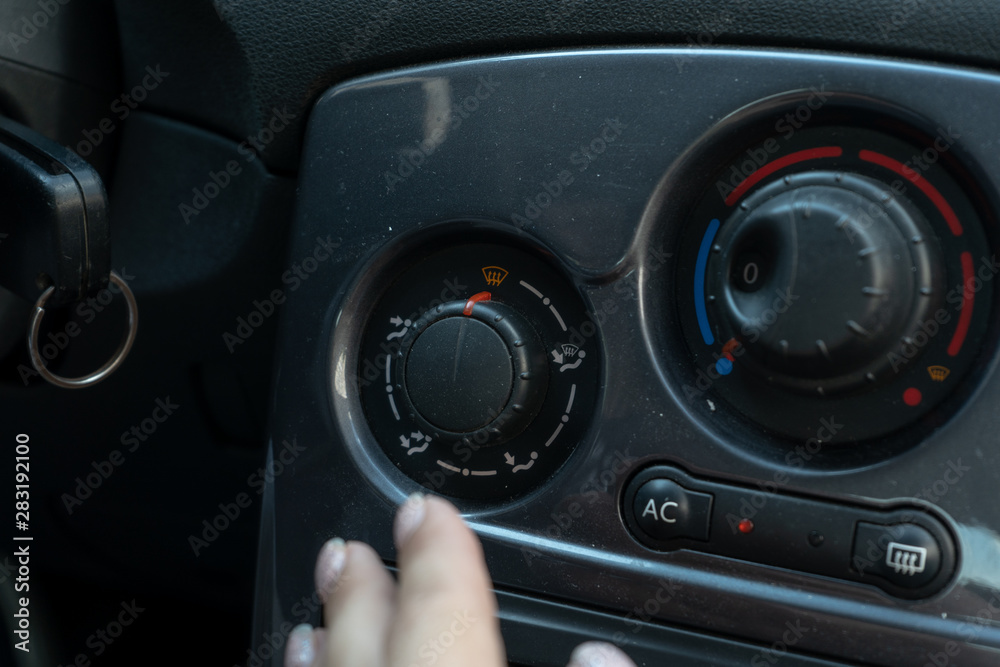 Woman hand reaches for the air conditioning mode knob on the panel in the car Woman hand reaches for the air conditioning mode knob on the panel in the car