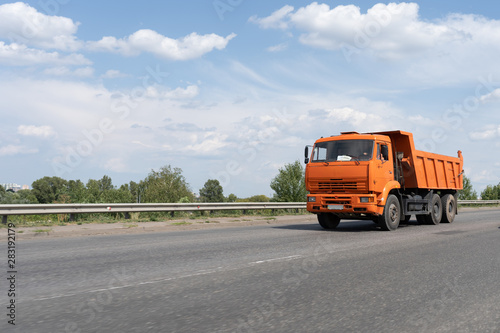 Orange garbage truck on the road against the blue cloudy sky on the summer day