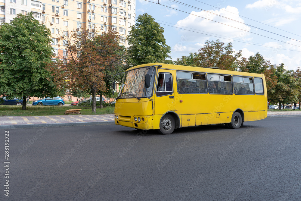 Fototapeta premium Yellow minibus rides on the paved city highway. The bus driver carries passengers along the route on a summer day