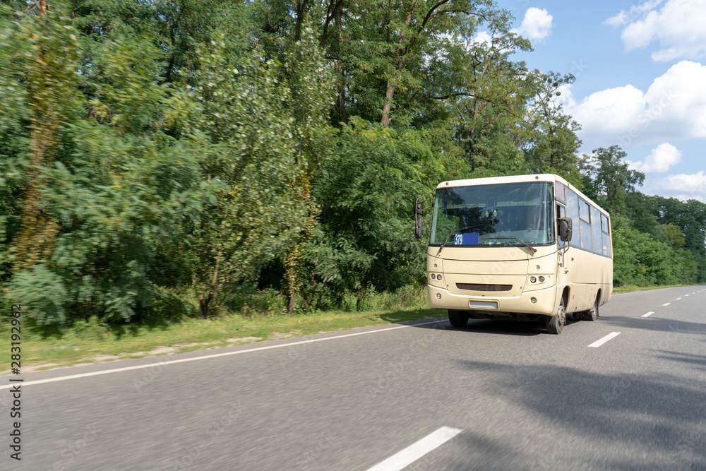 A minibus rides on an asphalt intercity highway through the forest. The bus driver carries passengers along the route on a summer day A minibus rides on an asphalt intercity highway through the forest. The bus driver carries passengers along the route on a summer day