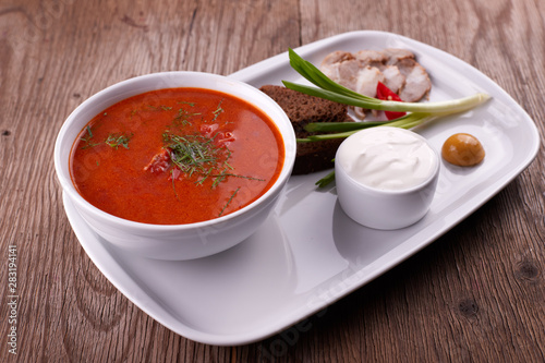 Ukrainian borsch with sour cream, onions and bacon on a white plate