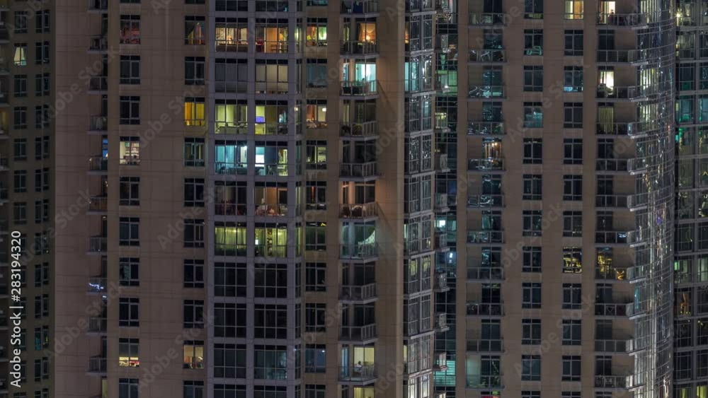 Windows of the multi-storey building with lighting inside and moving people in apartments timelapse. Aerial view of modern residential skyscrapers in Dubai downtown. Zoom out Windows of the multi-storey building with lighting inside and moving people in apartments timelapse. Aerial view of modern residential skyscrapers in Dubai downtown. Zoom out