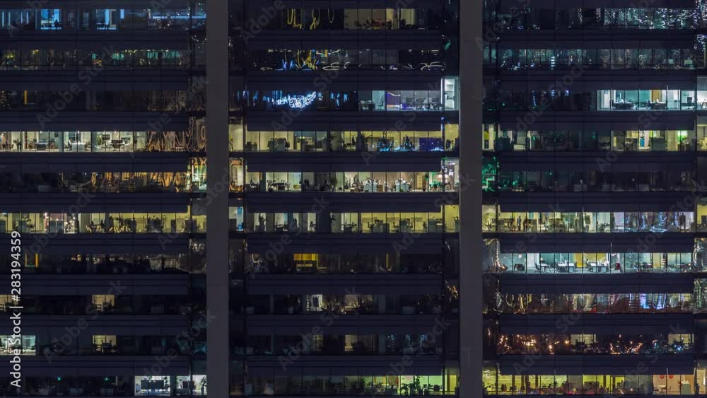 Office glowing windows on facade of a modern skyscraper showing business activity on each level of the building timelapse in the city. Zoom in Office glowing windows on facade of a modern skyscraper showing business activity on each level of the building timelapse in the city. Zoom in