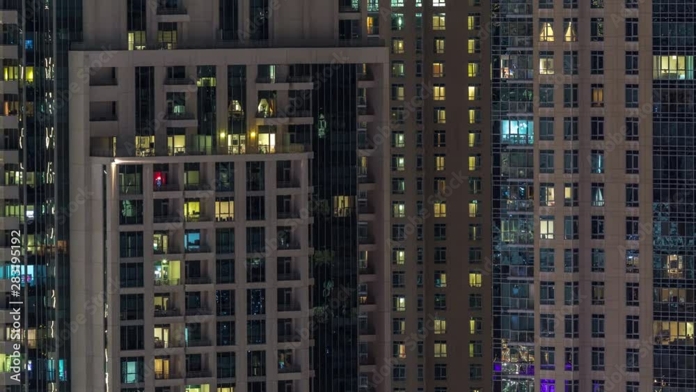 Windows of the multi-storey building with lighting inside and moving people in apartments timelapse. Aerial view of modern residential skyscrapers in Dubai downtown. Zoom out Windows of the multi-storey building with lighting inside and moving people in apartments timelapse. Aerial view of modern residential skyscrapers in Dubai downtown. Zoom out