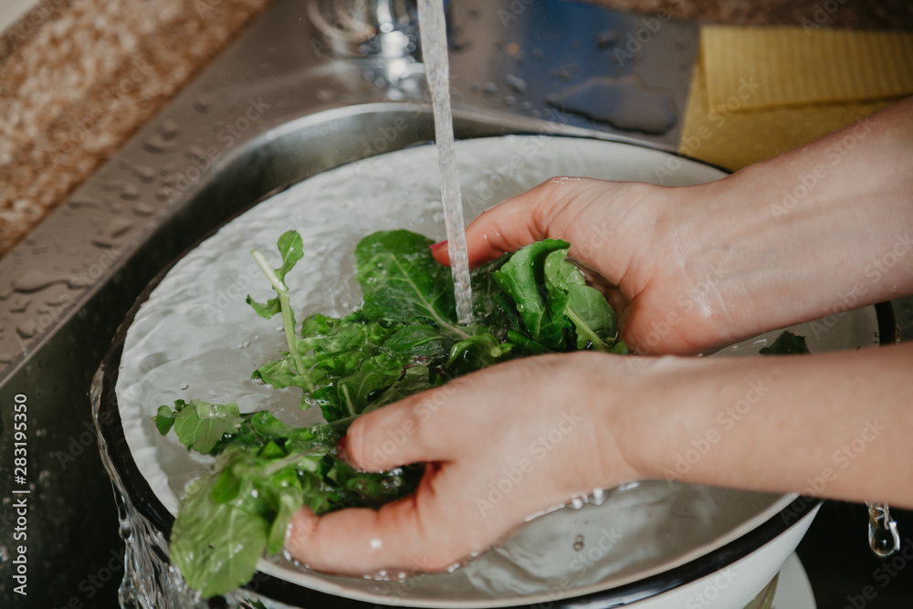 Hands of woman washing green leaves of arugula