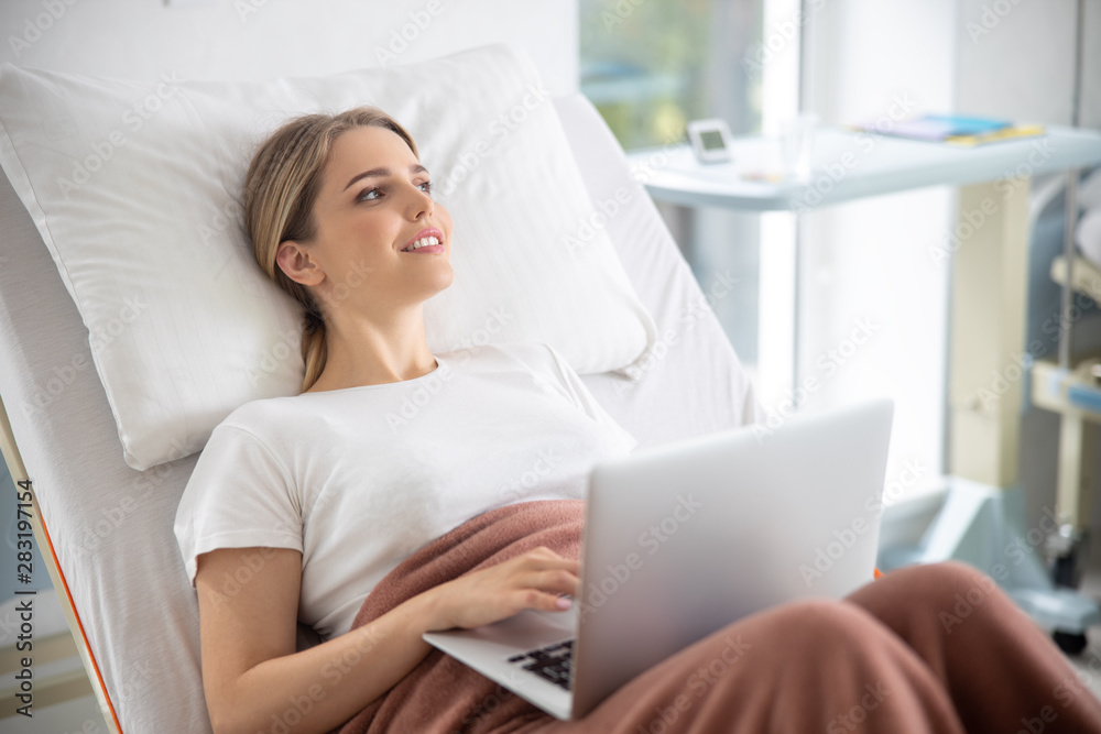 Smiling young woman using notebook in hospital room Smiling young woman using notebook in hospital room