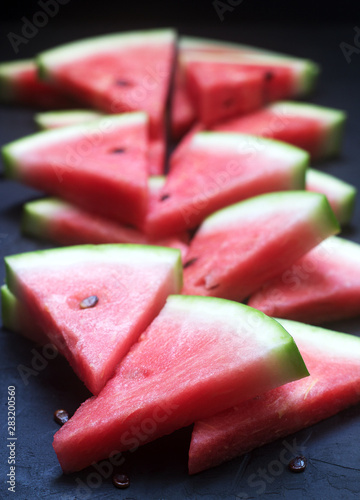 Triangular watermelon slices with seeds on a black concrete background.