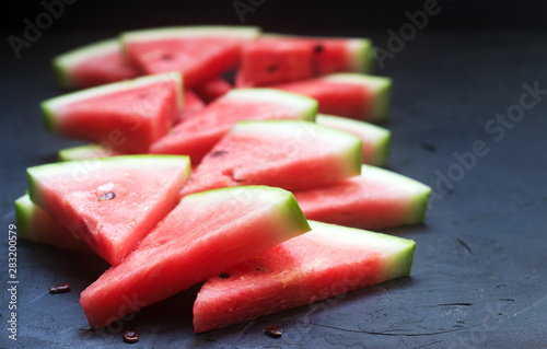 Triangular watermelon slices with seeds on a black concrete background.