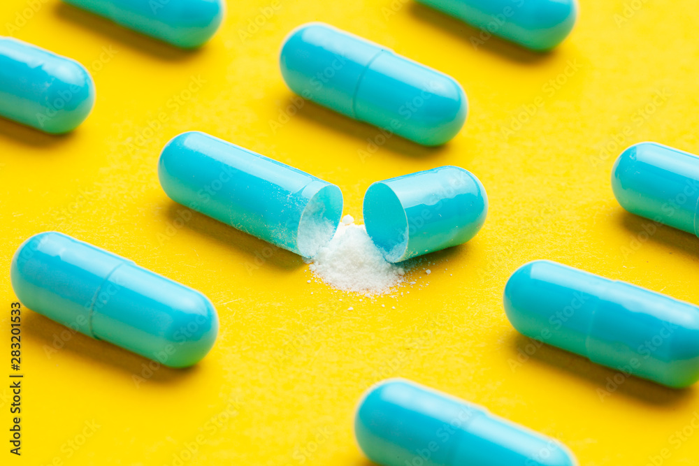 Blue tablets in capsules. One capsule is open. Yellow background. Blue tablets in capsules. One capsule is open. Yellow background.