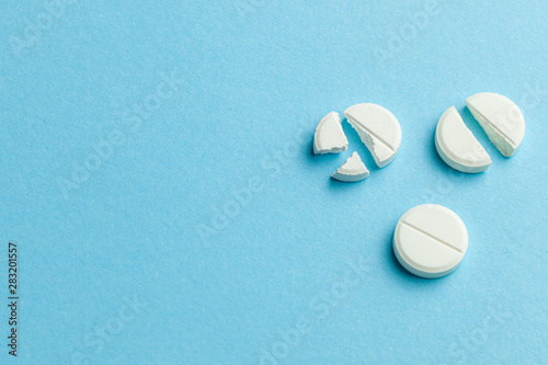 White pills on blue background. Few pills broken in half, reducing the dose of the medicine. Copy space for text.