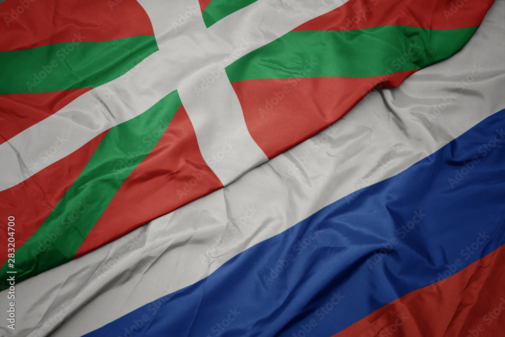 waving colorful flag of russia and national flag of basque country.