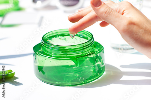 Womans hand is dipping finger in a cosmetic aloe vera gel in a transparent jar close up. After sun cooling skin cosmetics