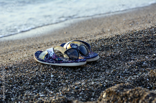 Dawn. On the sea beach near the water are beach shoes with sunglasses. Concept - sea vacation