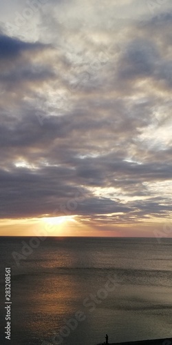 The autumn severe dark sea is illuminated by the setting sun  peeking through dense blue-gray clouds. Alarming and beautiful seascape. Dark gray clouds  solemn majestic sea and the golden setting sun.