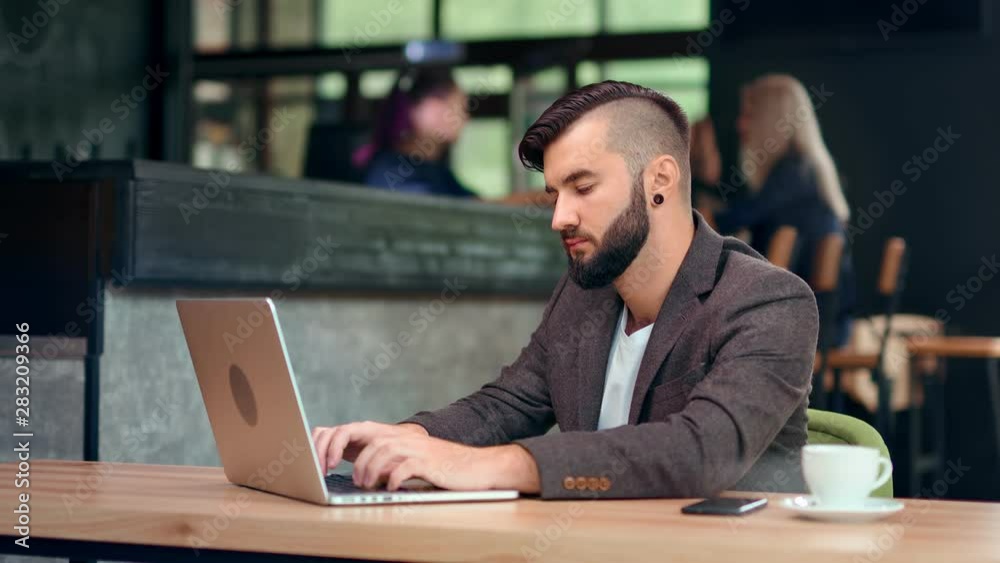 Handsome trendy male businessman chatting online using computer pc sitting on table at cafe