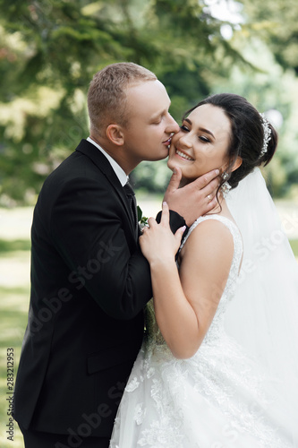 A very beautiful bride girl in a wedding dress embraces her stylish man. Kiss the bride is a stylish pair of models of the perfect man and the perfect girl. Amazing smiling wedding couple.