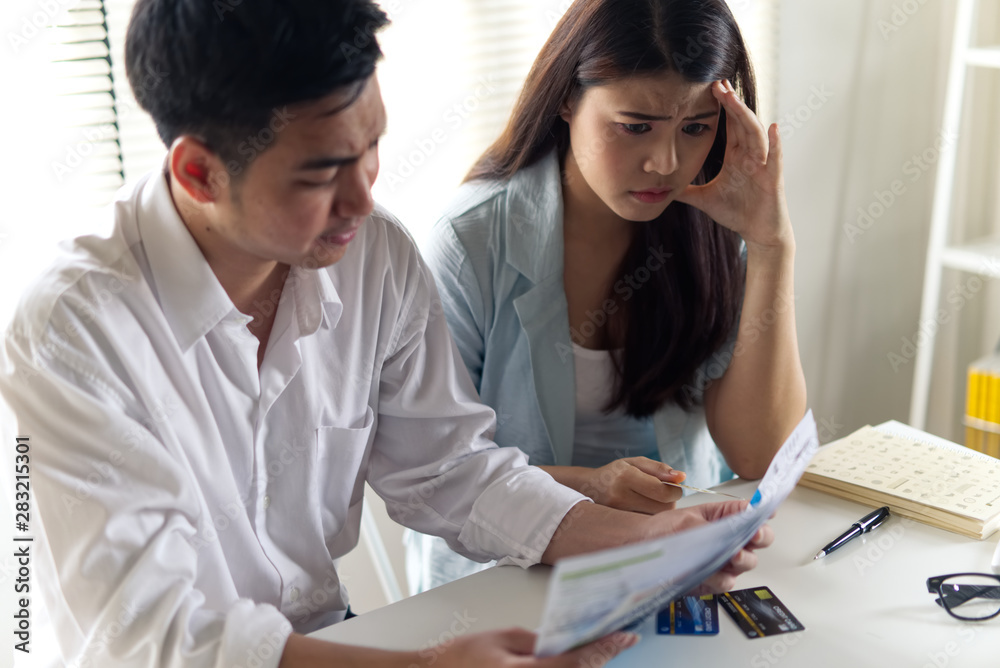 Fototapeta premium Stressed young Asian couples sitting with hands holding credit card and bills worry about find money to pay credit card debt and all loan bills. they are feeling stressful. Financial problem concept.