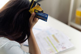 Top view of stressed young Asian woman hands holding the head with dummy credit cards trying to find money to pay credit card debt and all loan bills put on table. Financial problem concept.