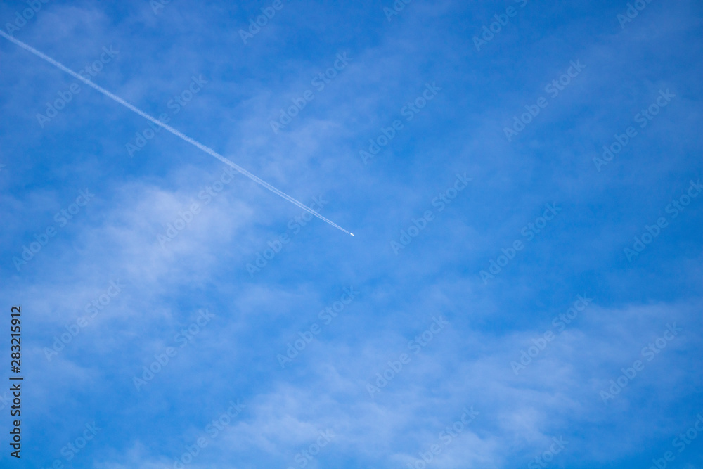 Airplane flying in the blue sky among clouds and sunlight