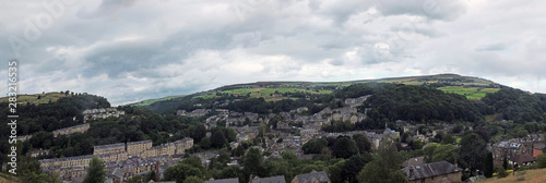 a wide panoramic view of the town of hebden bridge with hillside streets surrounded by trees and pennine fields