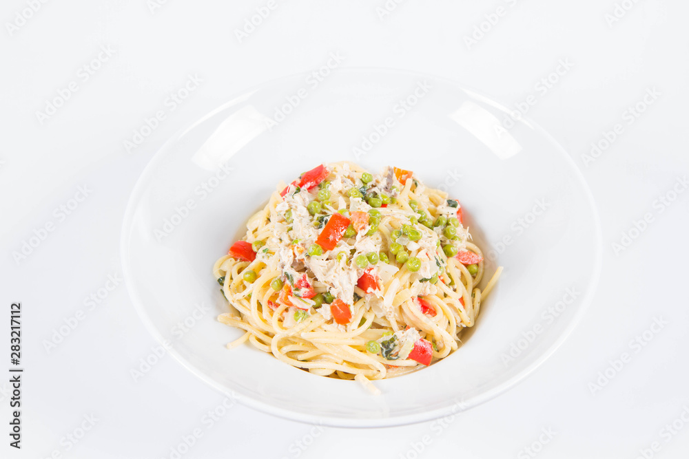 Spaghetti with cream sauce with smoked mackerel, peas ,bell pepper and some parsley on a white plate on a white background
