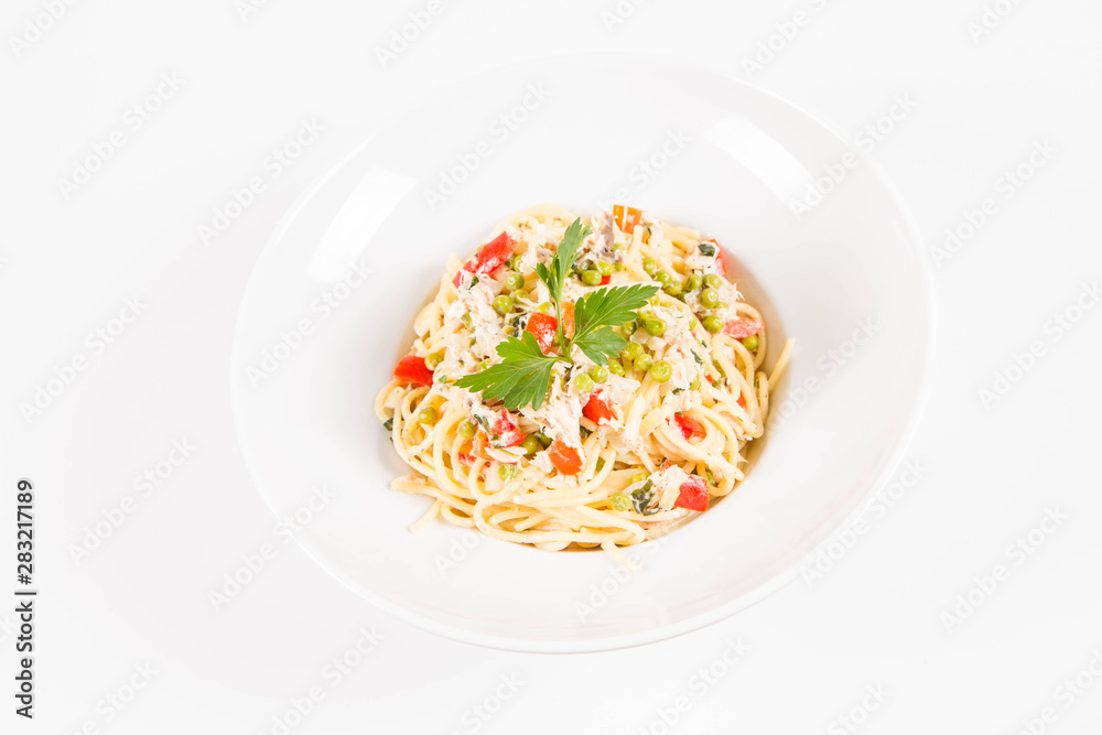 Spaghetti with cream sauce with smoked mackerel, peas ,bell pepper and some parsley on a white plate on a white background