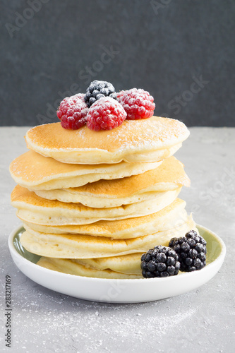 American pancakes with raspberries, blackberries and powdered sugar for breakfast on a gray concrete background with copy space