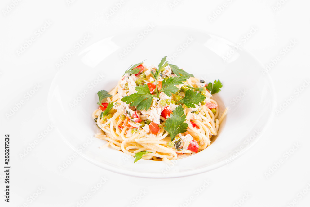 Spaghetti with cream sauce with smoked mackerel, peas ,bell pepper and some parsley on a white plate on a white background