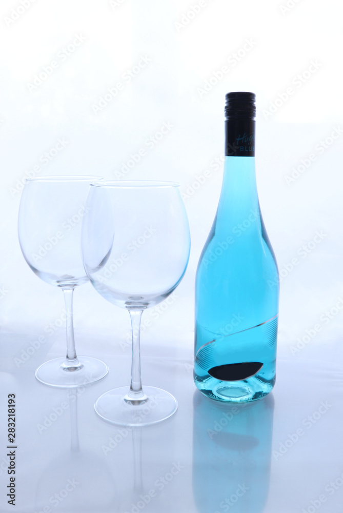 Wine bottle with blue wine next to two wine glasses against a white background with reflection of the glass. Wine bottle with blue wine next to two wine glasses against a white background with reflection of the glass.