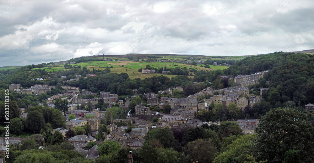 a wide panoramic view of the town of hebden bridge with hillside streets surrounded by trees and pennine fields