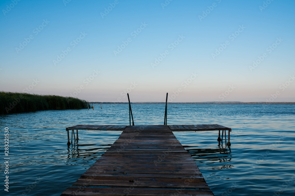 Fototapeta premium Wood deck over blue Balaton lake in Hungary at a cold morning at summertime, copy space.