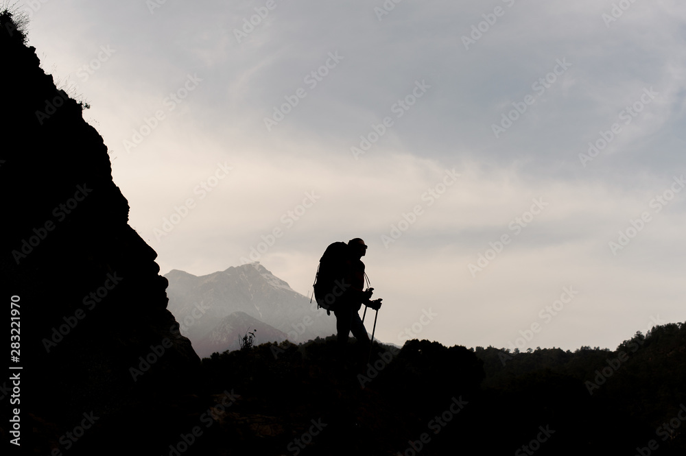 Dark silhouette woman standing on the rocks with hiking backpack and walking sticks