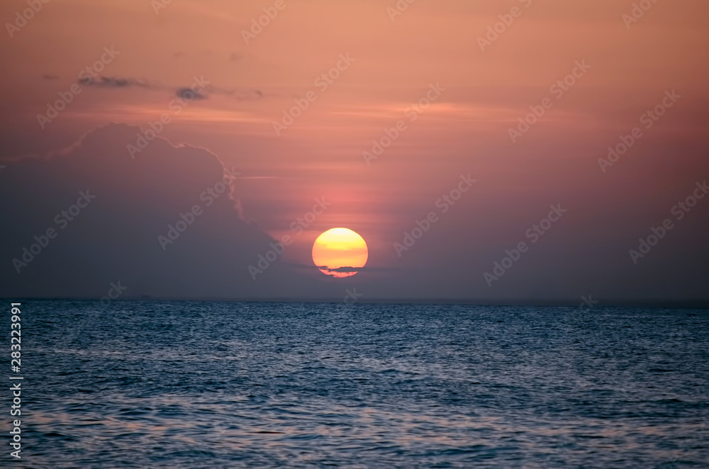 Закатное солнце над спокойной морской водой в розовых вечерних облаках