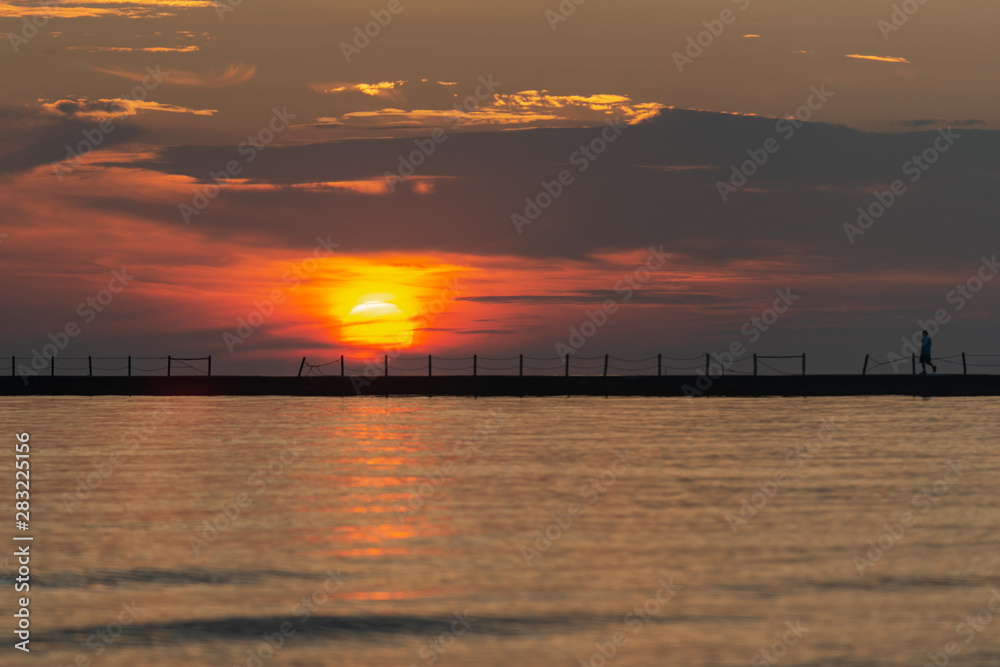 Silhouette of a walking man at a Pier at Sunrise with Sun reflecting in the Lake Michigan.