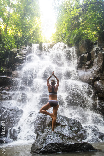 Woman practices yoga near waterfall in Bali  Indonesia