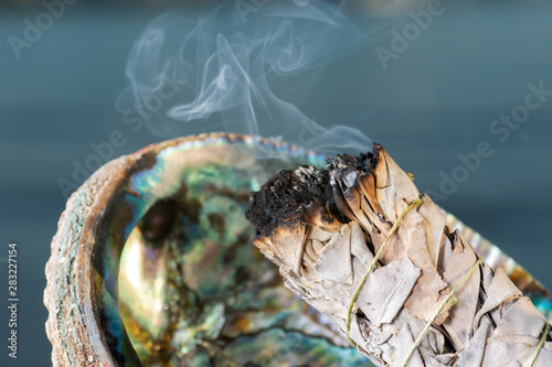 Smudging Ritual using burning thick leafy bundle of White Sage in bright polished Rainbow Abalone Shell on the beach at sunrise in front of the lake. photo