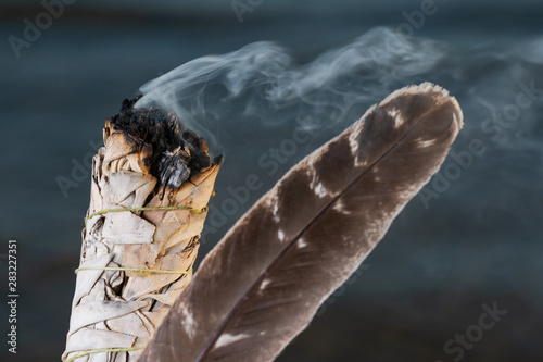 Smudging Ritual using burning thick leafy bundle of White Sage Grade A barred Turkey Smudging Feather on the beach at sunrise in front of the lake.