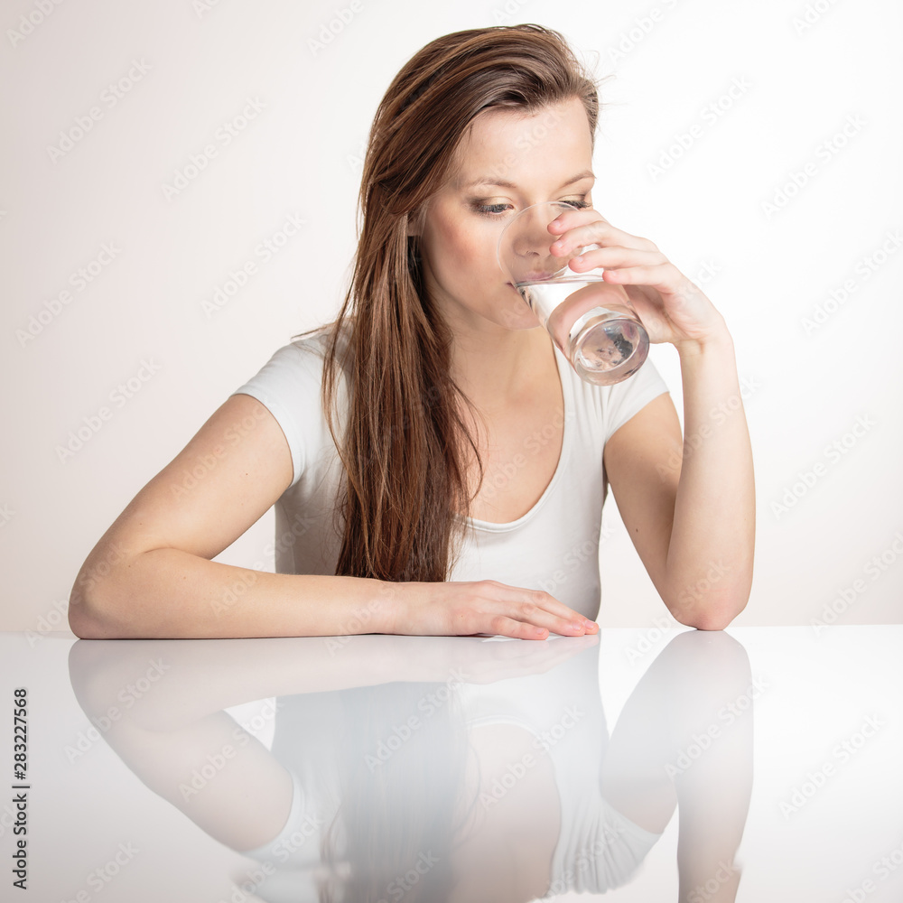 Beautiful, young woman isolated on white background with a reflection underneath her having a drink of clean, fresh water