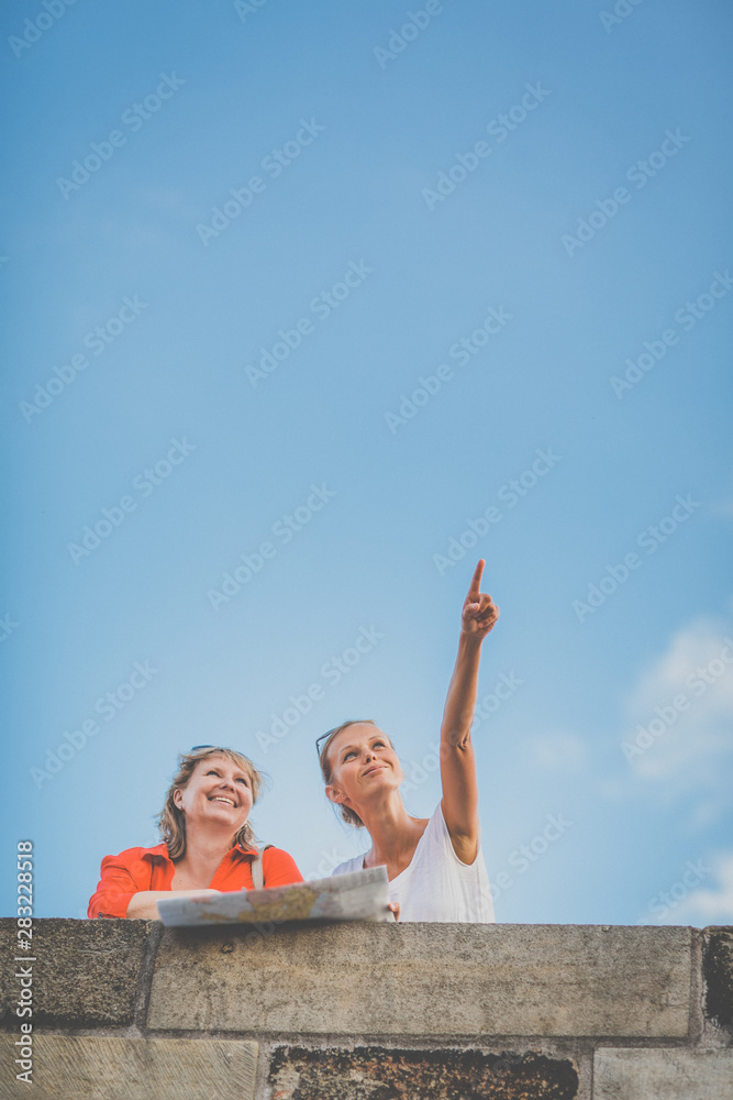 Fototapeta premium Mother and daughter traveling - two female tourists studying a map, discovering a new city