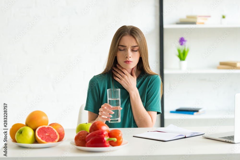 front view of woman with closed eyes holding glass of water and touching neck front view of woman with closed eyes holding glass of water and touching neck