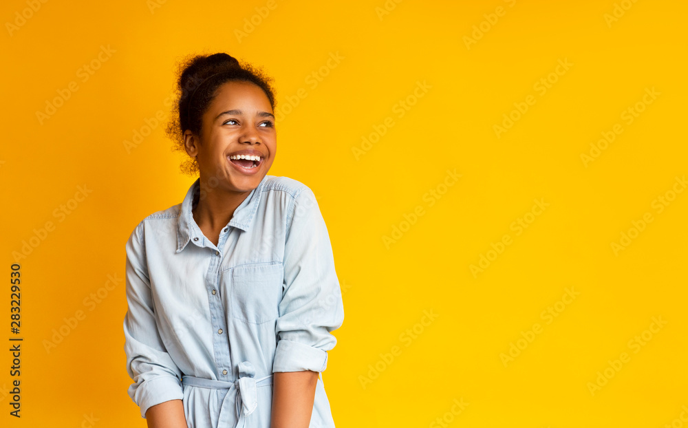 Excited black teen looking upwards standing against yellow studio background - obrazy, fototapety, plakaty 