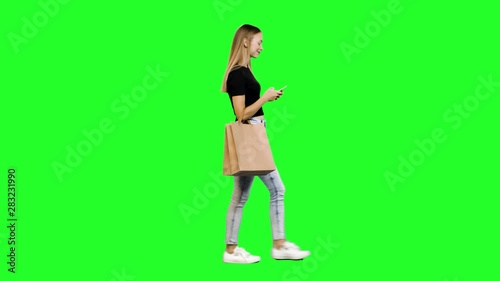 Taking a Selfie or using an app while walking, a casual young woman with shopping bags over green screen.