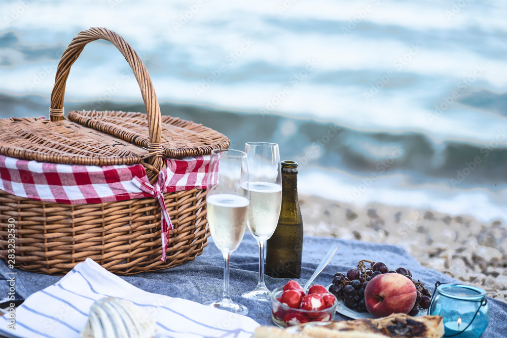 Summer beach  romantic picnic at sunset. Seaside light evening picnic  with fresh fruit and tray of tasty appetizers,  glasses with sparkling wine