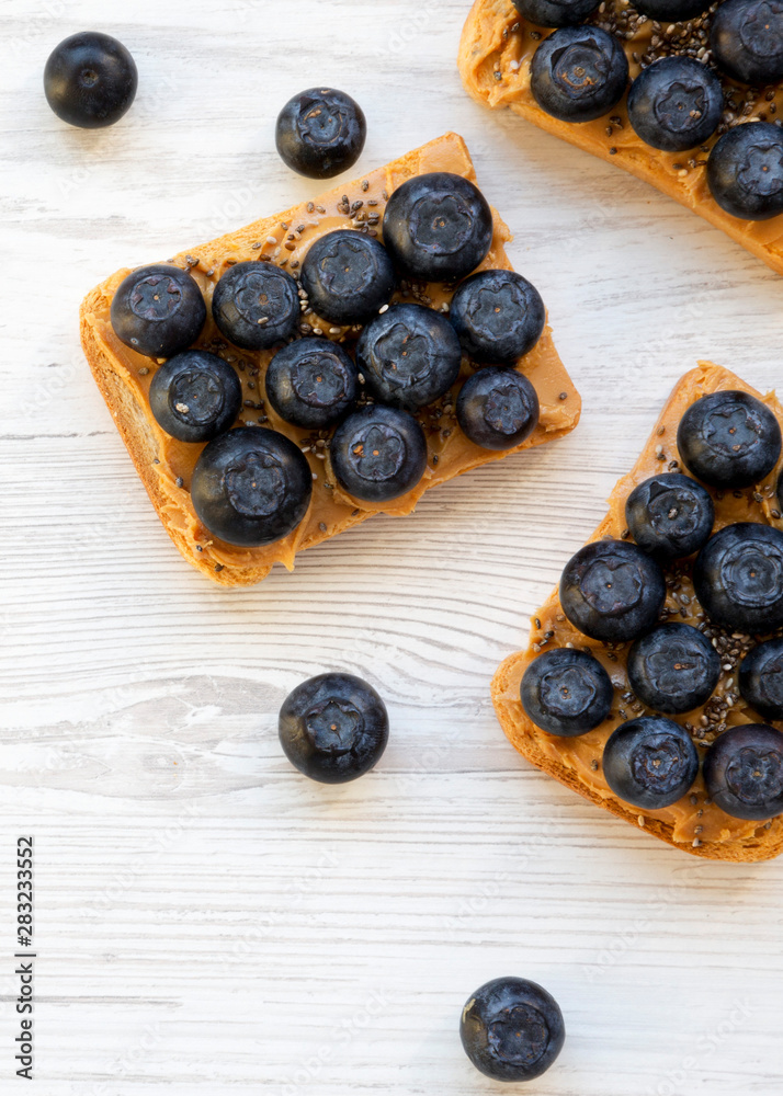 Vegan toasts with peanut butter, blueberries and chia seeds on a white wooden background, overhead view. Healthy eating. Flat lay, from above, top view. Vegan toasts with peanut butter, blueberries and chia seeds on a white wooden background, overhead view. Healthy eating. Flat lay, from above, top view.