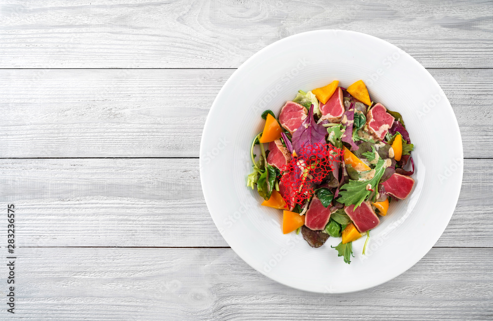 Healthy salad with seared tuna fish, greens, bell pepper and sauce in plate on light wooden background. Healthy food, clean eating, dieting, top view Healthy salad with seared tuna fish, greens, bell pepper and sauce in plate on light wooden background. Healthy food, clean eating, dieting, top view