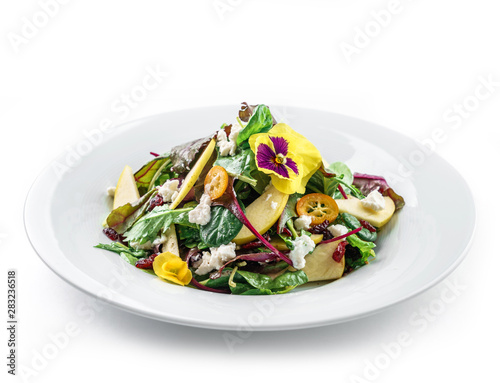 Healthy fresh salad with mix greens, apple, cream cheese, cranberry, sauce and edible flowers in plate on isolated white background. Healthy food, vegetarian dieting