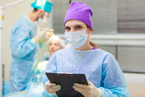 Beautiful portrait of a doctor with documents on the background of the operating room. Baldness treatment. Hair transplant. Surgeons in the operating room carry out hair transplant surgery. Surgical