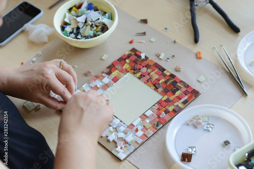 Process of making a mosaic picture from ceramic tile. The man organizes with a tweezers a puzzle of ceramic elements to build a picture.